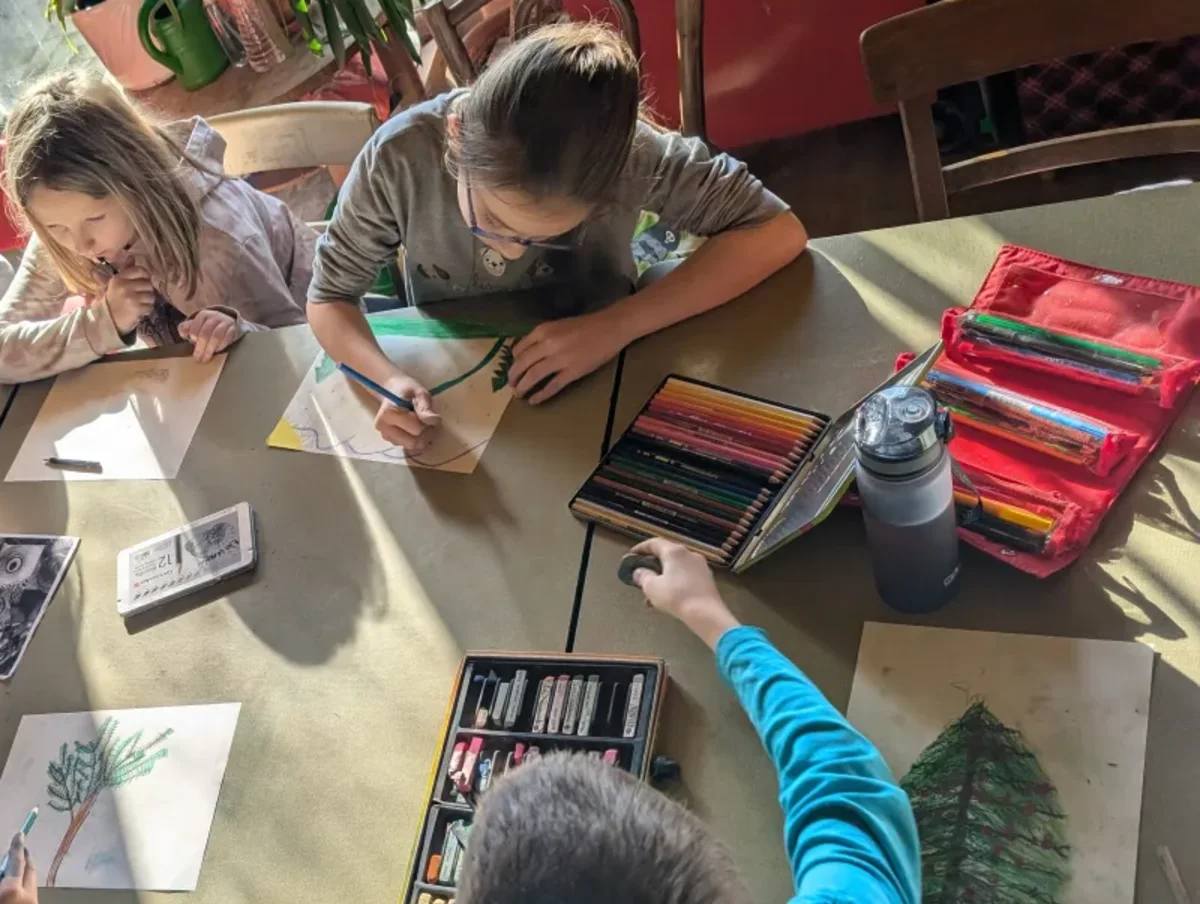 Drei Kinder zeichnen mit Farbstiften an einem großen Ateliertisch